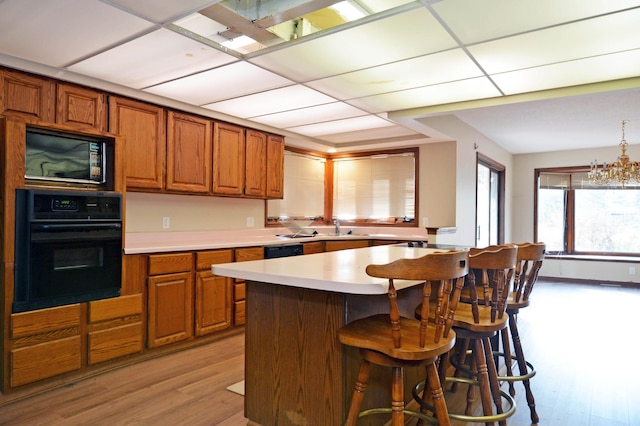 kitchen with a kitchen breakfast bar, light wood-type flooring, black appliances, a notable chandelier, and sink