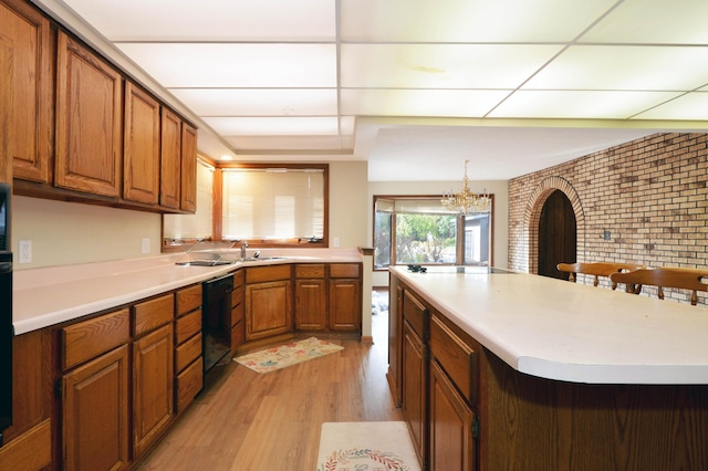 kitchen featuring hanging light fixtures, a kitchen bar, black appliances, light hardwood / wood-style floors, and brick wall