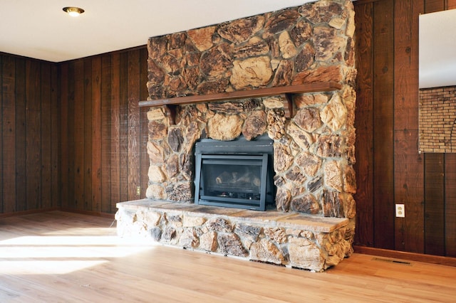 details with hardwood / wood-style floors, wooden walls, and a stone fireplace