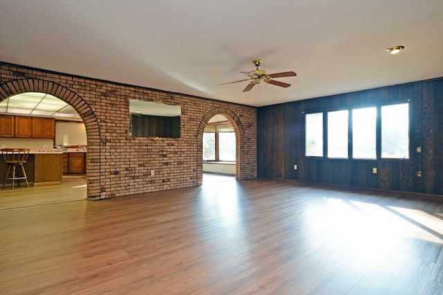 unfurnished living room with brick wall, a textured ceiling, light wood-type flooring, and ceiling fan