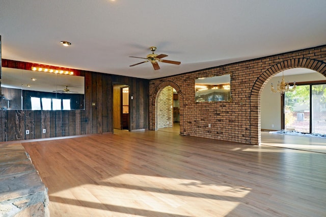 unfurnished living room with brick wall, hardwood / wood-style flooring, a healthy amount of sunlight, and wood walls