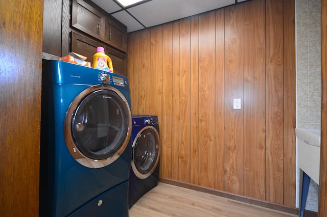 laundry room featuring wooden walls, light hardwood / wood-style flooring, independent washer and dryer, and cabinets