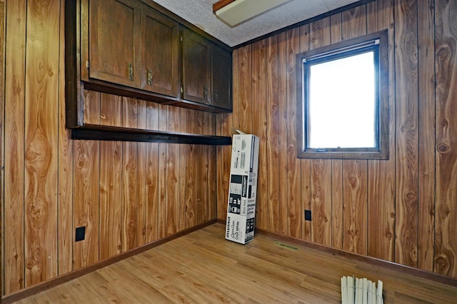 interior space with a textured ceiling, light hardwood / wood-style floors, and wood walls