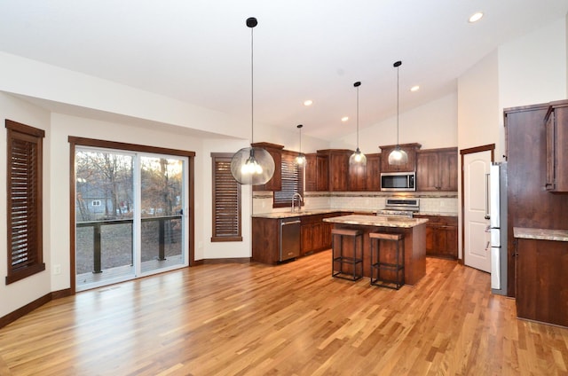 kitchen with appliances with stainless steel finishes, a center island, decorative light fixtures, a kitchen breakfast bar, and backsplash