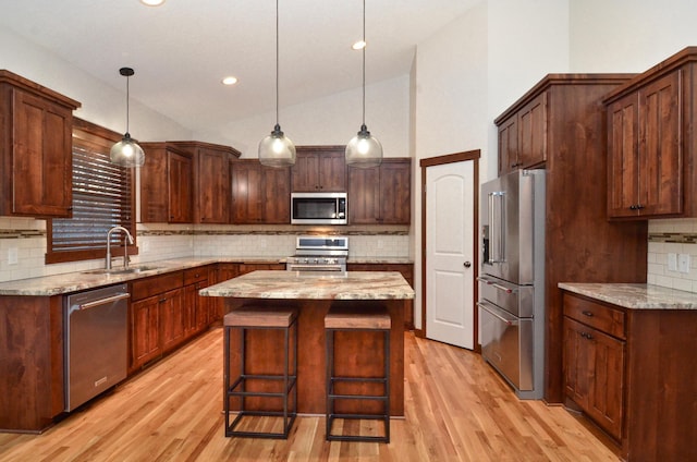 kitchen featuring lofted ceiling, a kitchen island, stainless steel appliances, sink, and light stone counters