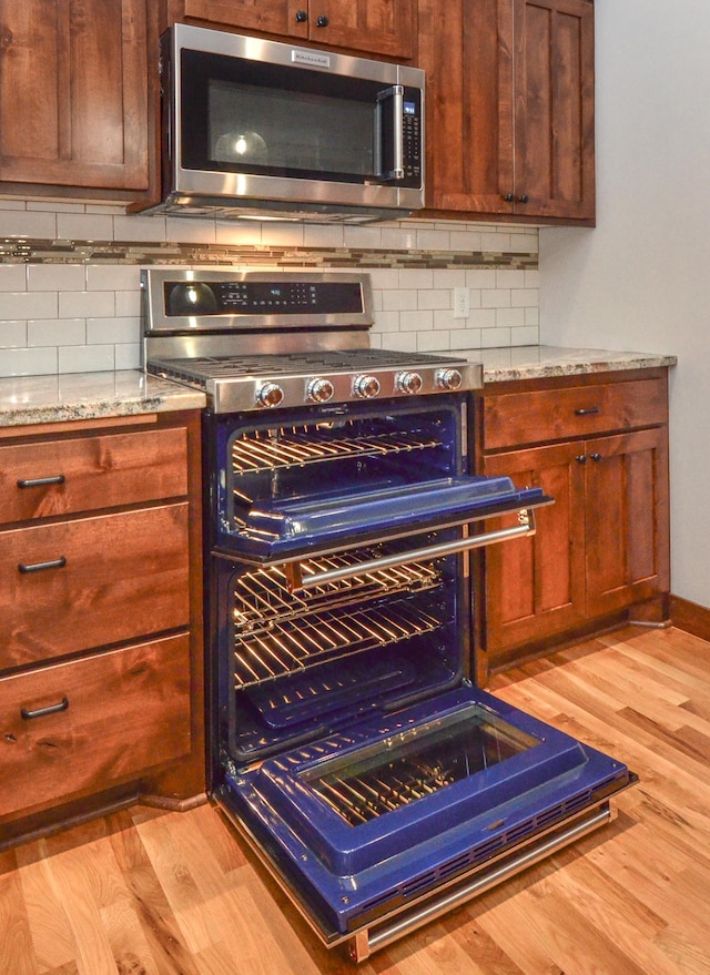 kitchen featuring light stone counters, light hardwood / wood-style floors, decorative backsplash, and stove