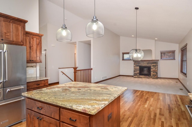 kitchen featuring decorative light fixtures, high quality fridge, lofted ceiling, a fireplace, and a center island