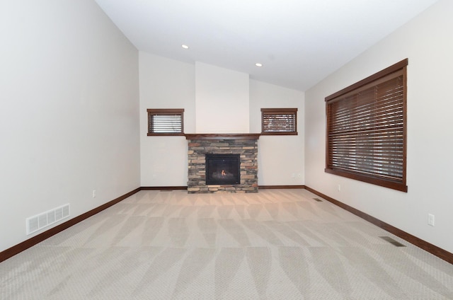 unfurnished living room with vaulted ceiling, light colored carpet, and a stone fireplace