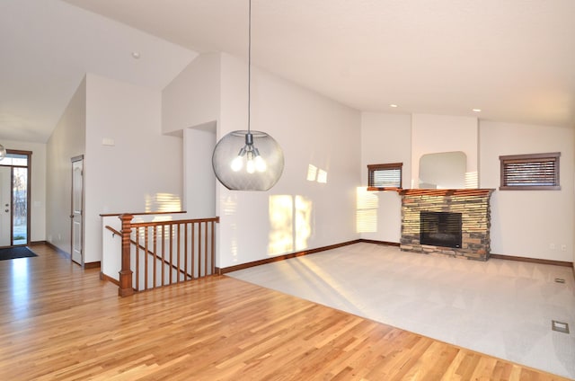 unfurnished living room with high vaulted ceiling, a stone fireplace, and baseboards