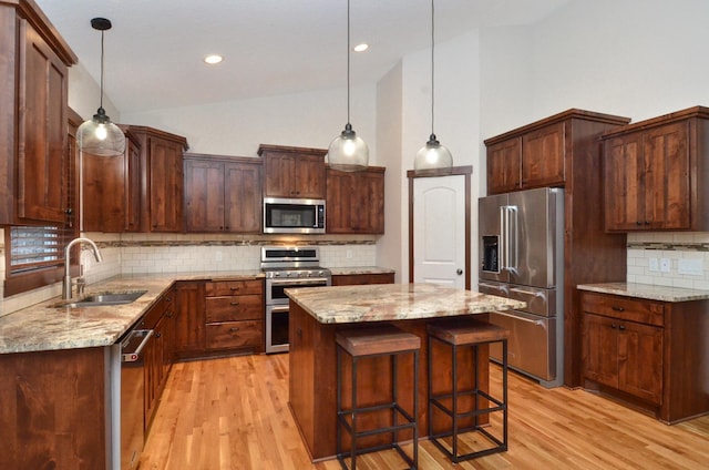 kitchen featuring light stone counters, hanging light fixtures, appliances with stainless steel finishes, a kitchen island, and a sink