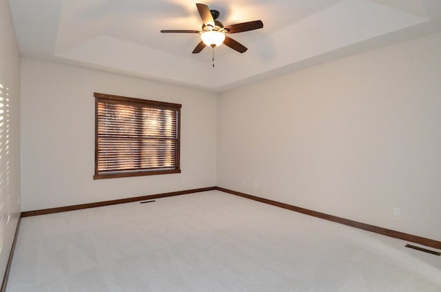 unfurnished room with ceiling fan, light carpet, visible vents, baseboards, and a raised ceiling