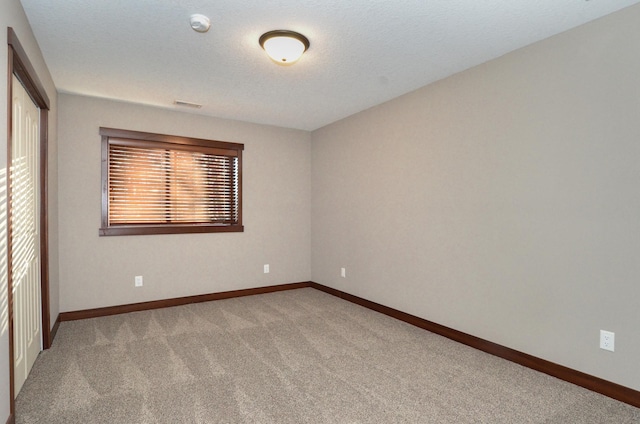 empty room with light carpet, a textured ceiling, and baseboards