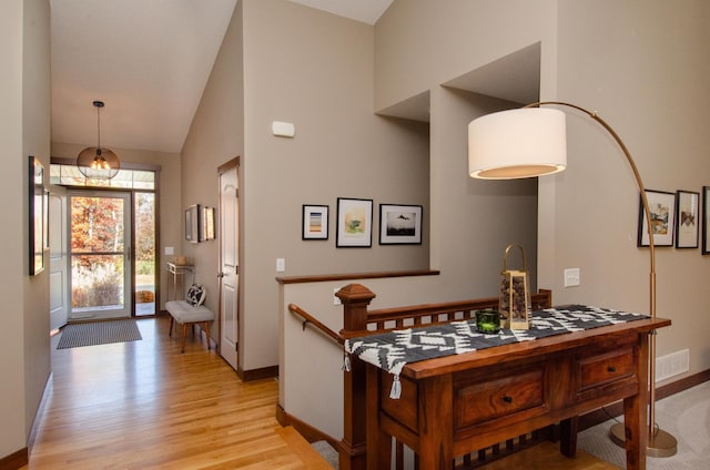 interior space with high vaulted ceiling, light wood-type flooring, visible vents, and baseboards