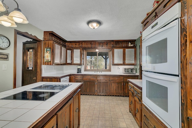 kitchen with a textured ceiling, white appliances, sink, tile countertops, and decorative light fixtures