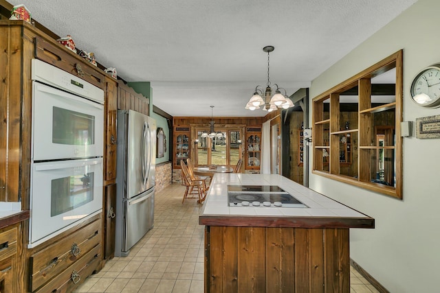 kitchen featuring black electric stovetop, white double oven, a chandelier, a center island, and stainless steel refrigerator