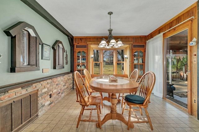 tiled dining room with wooden walls, brick wall, and an inviting chandelier