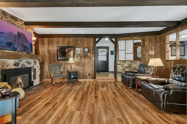 living room featuring beam ceiling, a stone fireplace, wood walls, and hardwood / wood-style flooring