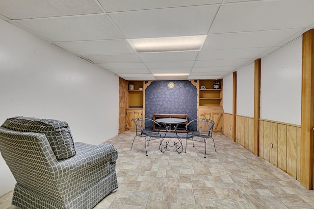 living area with wooden walls and a drop ceiling