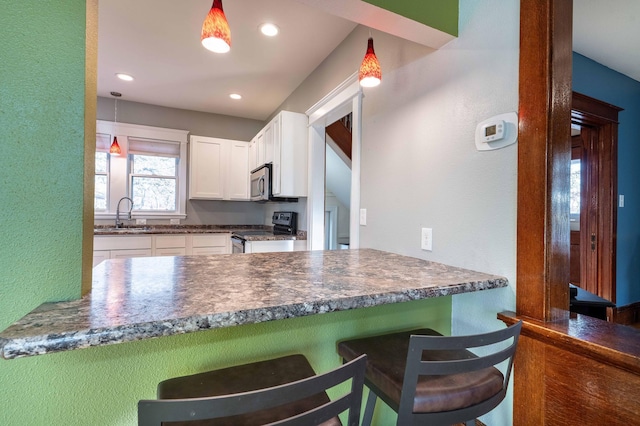 kitchen featuring a breakfast bar area, hanging light fixtures, sink, black / electric stove, and white cabinets