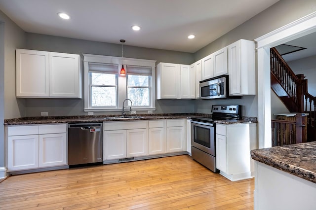 kitchen featuring stainless steel appliances, sink, decorative light fixtures, light wood-type flooring, and white cabinetry