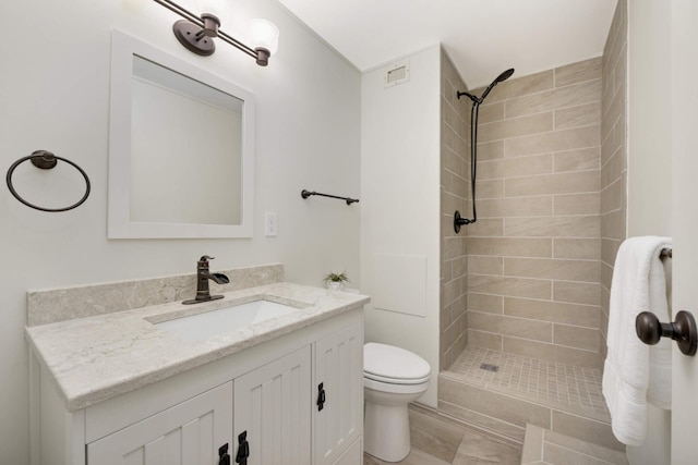 bathroom featuring vanity, toilet, a tile shower, and tile patterned flooring