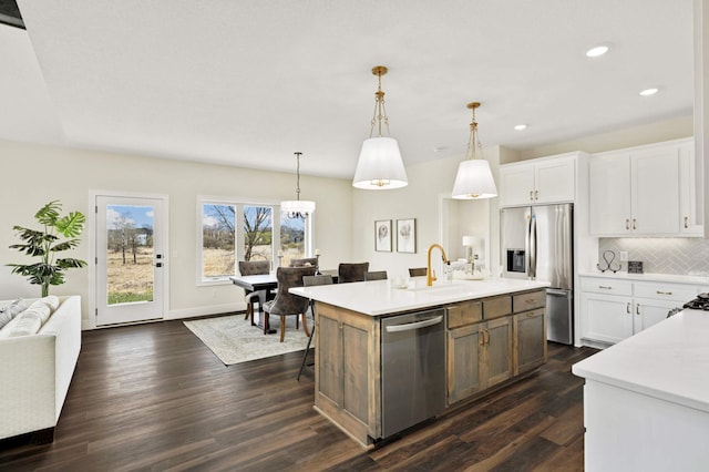 kitchen featuring white cabinets, appliances with stainless steel finishes, a center island with sink, and decorative light fixtures