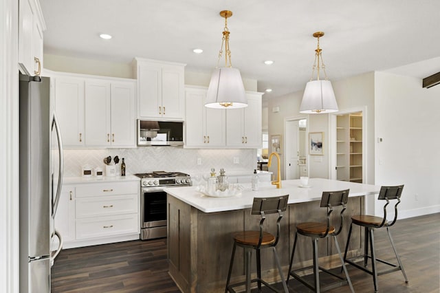 kitchen with a kitchen island with sink, stainless steel appliances, white cabinetry, and dark hardwood / wood-style floors