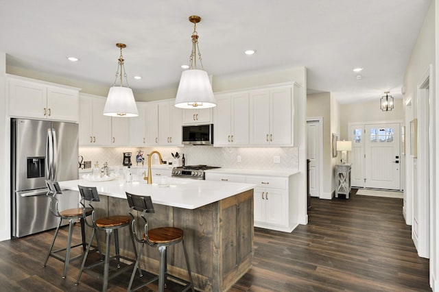 kitchen with stainless steel appliances, pendant lighting, a kitchen island with sink, dark hardwood / wood-style floors, and white cabinetry