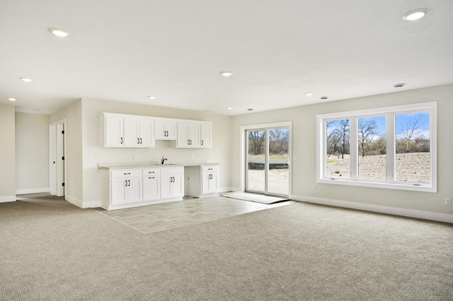 unfurnished living room featuring sink, light colored carpet, and plenty of natural light