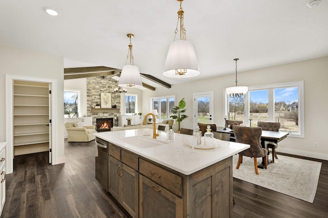 kitchen with sink, dark hardwood / wood-style floors, an island with sink, a stone fireplace, and dishwasher