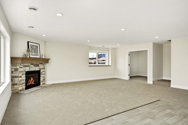 unfurnished living room featuring a stone fireplace and light colored carpet