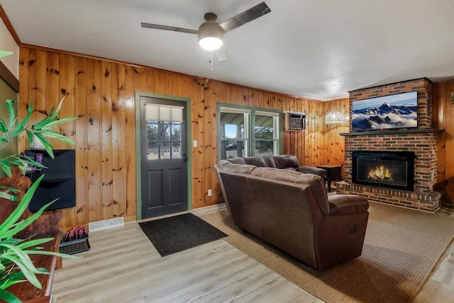 living room with light hardwood / wood-style flooring, a fireplace, ceiling fan, and wood walls