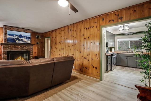 living room featuring a brick fireplace, light hardwood / wood-style flooring, wooden walls, and ceiling fan