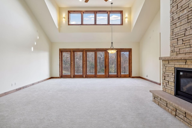 unfurnished living room featuring a high ceiling, a stone fireplace, light carpet, and ceiling fan