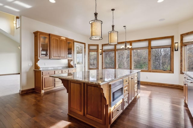 kitchen featuring pendant lighting, stainless steel microwave, light stone counters, a kitchen island, and dark hardwood / wood-style flooring