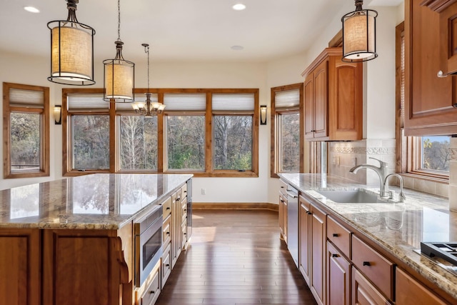 kitchen with pendant lighting, sink, stainless steel appliances, light stone counters, and a kitchen island