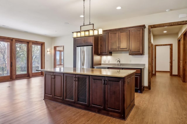 kitchen with decorative light fixtures, a center island, dark brown cabinets, light wood-type flooring, and stainless steel fridge