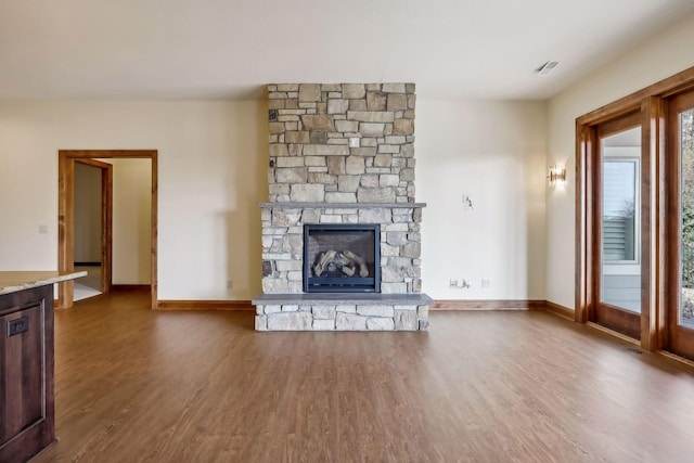 unfurnished living room with a stone fireplace and dark wood-type flooring