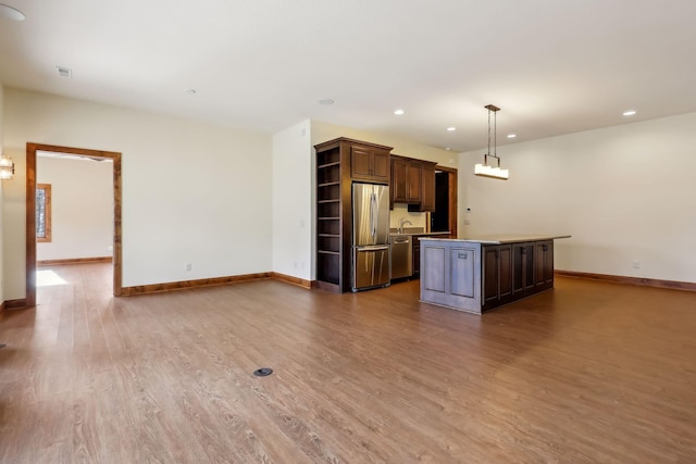 kitchen with pendant lighting, hardwood / wood-style flooring, stainless steel appliances, dark brown cabinetry, and a kitchen island