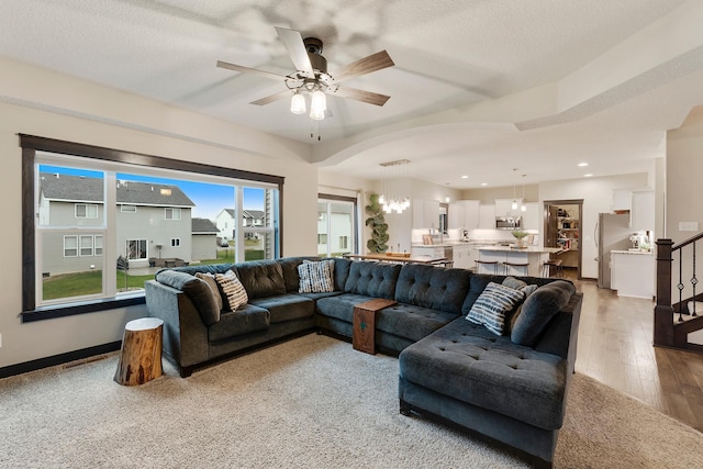 living room with ceiling fan with notable chandelier, light wood-type flooring, and a textured ceiling