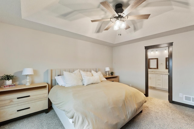 bedroom with light carpet, ensuite bathroom, ceiling fan, and a tray ceiling