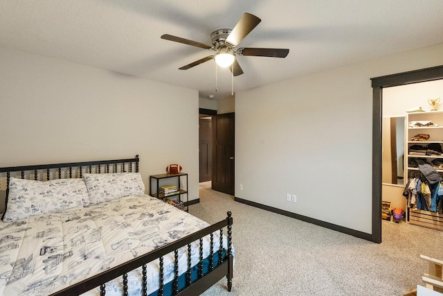 carpeted bedroom featuring a walk in closet and ceiling fan