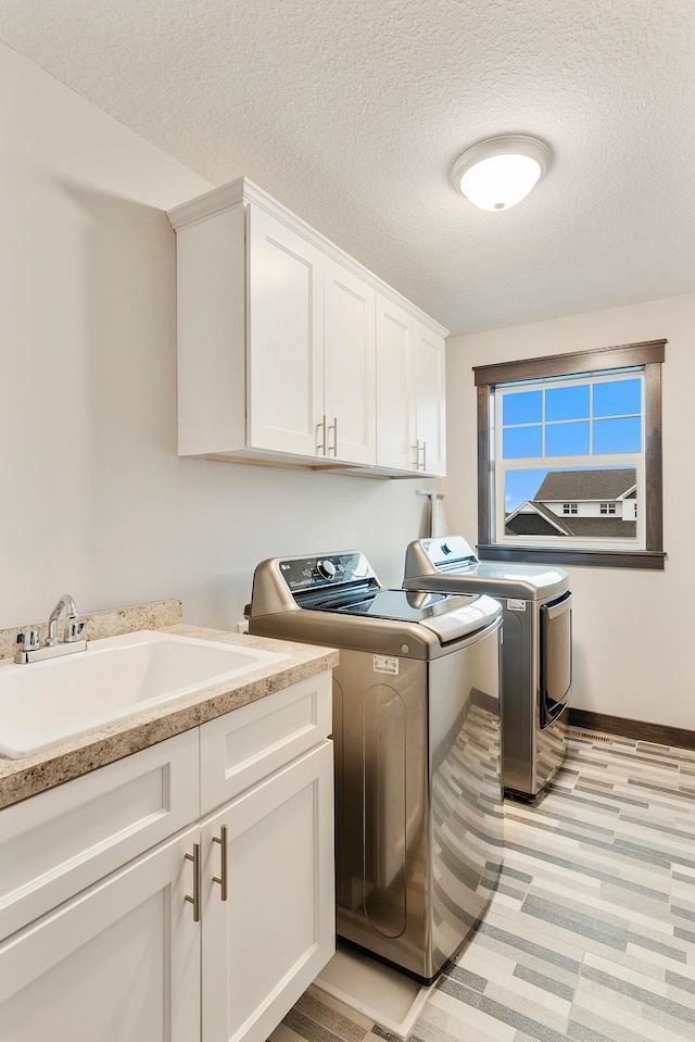 laundry room with washer and dryer, a textured ceiling, cabinets, and sink