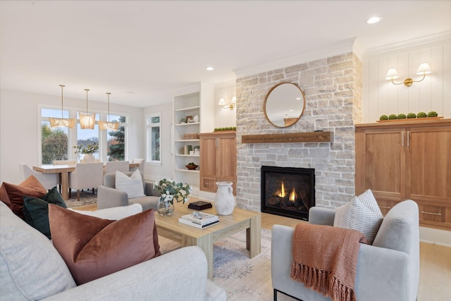 living room featuring a stone fireplace, light wood-type flooring, ornamental molding, and built in shelves