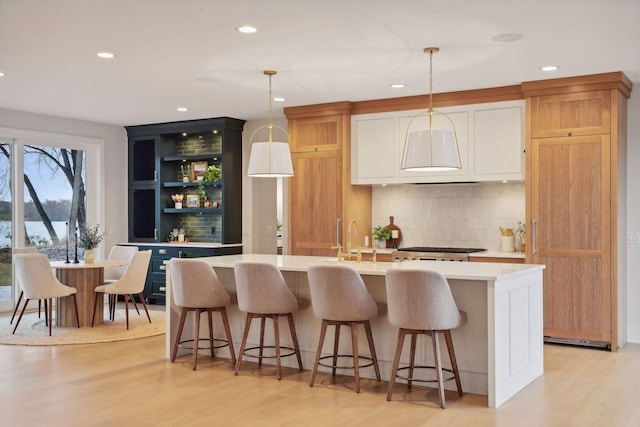 kitchen with a kitchen island with sink, light hardwood / wood-style flooring, and hanging light fixtures