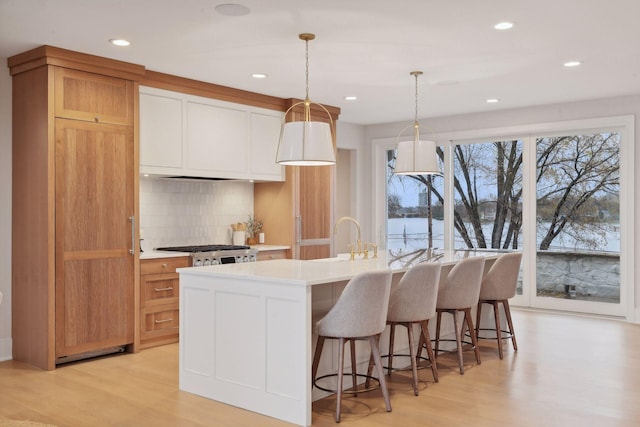 kitchen featuring light hardwood / wood-style floors, stainless steel stove, a kitchen island with sink, and decorative light fixtures