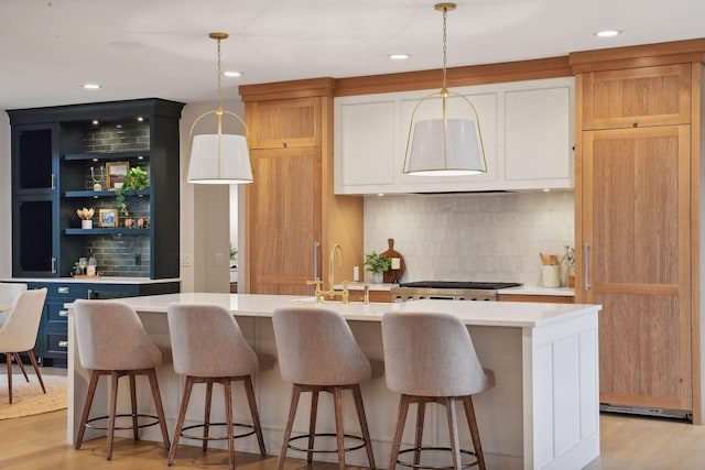 kitchen with backsplash, light hardwood / wood-style floors, decorative light fixtures, and a center island with sink