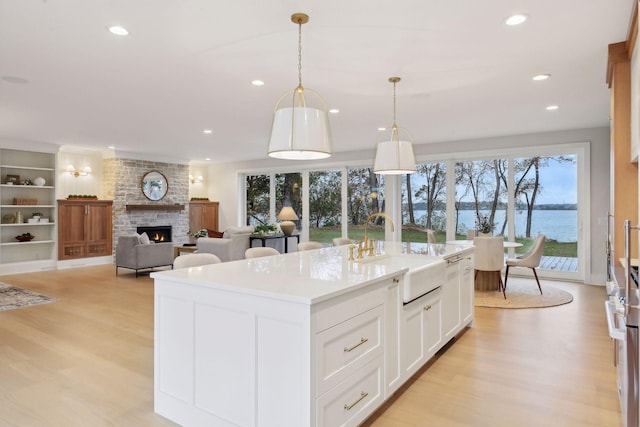 kitchen featuring white cabinetry, decorative light fixtures, sink, a water view, and a kitchen island with sink