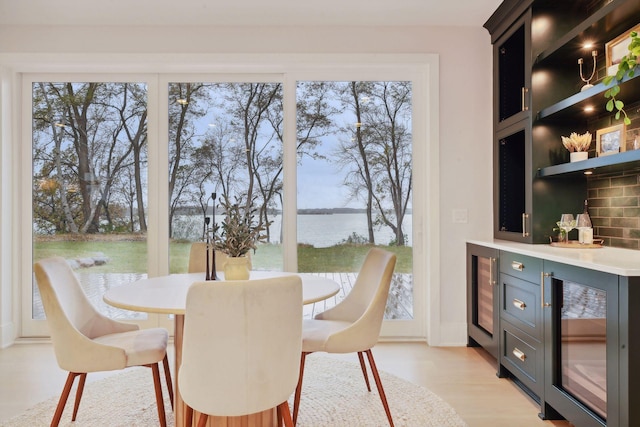 dining area featuring wine cooler, a water view, and light hardwood / wood-style flooring