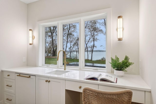 kitchen featuring white cabinetry, a water view, sink, and built in desk